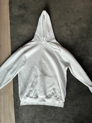 Vit hoodie med magficka och huva - Snygg vit hoodie med klassisk magficka och dragsko i huvan. Hoodien har ribbade muddar vid ärmslut och nederkant. Perfekt för en chill och avslappnad stil. Materialet känns mjukt och bekvämt mot huden.