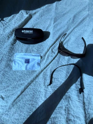 Polaroid sportiga solglasögon svart - Säljer ett par sportiga solglasögon från Polaroid i svart med breda bågar och svepande form. Kommer med originalfodral och putsduk. Perfekta för dig som vill ha en cool och funktionell look i solen.