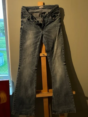 Blå bootcut jeans med slitningar - Säljer ett par blå bootcut jeans med snygga slitningar och tvättad look. Jeansen är rätt skadade vid midjan, en av fickorna saknar knapp och har lite slit längst nere vid byxorna. Skriv gärna angående fler bilder eller information om skadorna och priset går att prata om. Förutom skadorna är byxorna super snygga och bekväma, säljer bara för att de inte passar mig längre. Passar perfekt för dig som gillar en avslappnad men trendig stil.