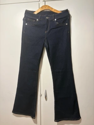 Mörkblå bootcut jeans med kontrastsömmar - Snygga mörkblå bootcut jeans med kontrastsömmar. Jeansen har dekorativa ficklock bak med knappdetaljer. Helt nya, aldrig använt pågrund av att dem är för småa. Passar säkert storlek M också.