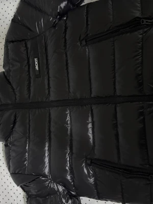 Svart pufferjacka från Jackit - Snygg svart pufferjacka från Jackit med glansig finish och raka quiltade sömmar. Jag köpte jackan för 2500 nypris och säljer den för detta priset. Vid snabbköp var gärna säkra och prisförslag är alltid välkomna.