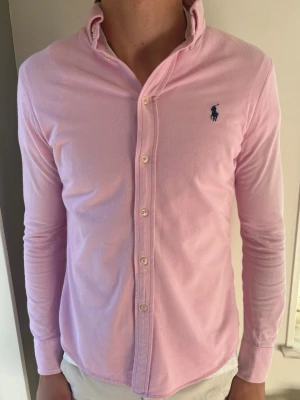 Rosa Ralph Lauren Featherweight Mesh Skjorta - Snygg rosa skjorta från Ralph Lauren i Featherweight Mesh. Riktigt go kvalitet! Passar perfekt nu till både vår och sommar. 🧵 Märke & Modell: Ralph Lauren 📏 Storlek: L men sitter  som en M/S. Vänligen mät noga! 🧩 Material: 100% ren bomull 📐 Mått: Axel 40 cm, armhåla 50 cm, ärm 64,5 cm, längd 69 cm ✅ Skick: 9/10. Väldigt fint skick! Bilderna talar. 🧍‍♂️Modellen (189 cm) bär den för tight. Passar en kortare!! Tips: Ta en skjorta du gillar och jämför måtten så det blir rätt. ‼️ Skickas iväg inom 24h ‼️