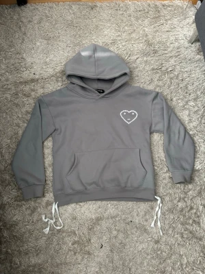 Grå hoodie från carsicko - Grå hoodie med huva och vita snören i nederkanten från carsicko. På bröstet finns ett vitt hjärta med små prickar runtom. Hoodien har magficka och långa ärmar, perfekt för en avslappnad stil. Passar perfket med de matchande byxorna. Hela setet/tracksuiten finns i min profil som en egen annons