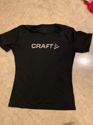 Svart tränings-tshirt från Craft - Snygg svart tränings-tshirt från Craft med logga i vitt på bröstet. T-shirten har rund hals, korta ärmar och är gjord i ett lätt och snabbtorkande funktionsmaterial som passar perfekt till träning och sport.