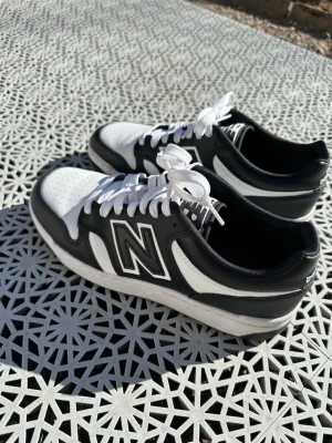 Svarta och vita New Balance sneakers - Snygga sneakers från New Balance i svart och vitt med klassisk N-logga på sidan. Skorna har lågt skaft, vita snören och perforerad tå för extra ventilation. Perfekta för dig som gillar streetwear och sportig stil. Använda 2 gånger inga defekter 