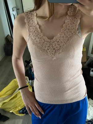 Ljusrosa ribbad linnetopp med spets - Supersöt ljusrosa linnetopp med bred spetskant och v-ringning. Toppen är ribbad och har en figurnära passform som framhäver siluetten. Perfekt att styla med jeans eller kjol för en trendig look.