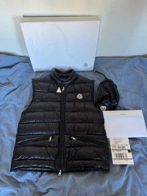 Svart dunväst från Moncler - En snygg moncler gui väst i storlek 2 vilket motsvarar ungefär S. Västen är i mycket bra skick och inte använd alls mycket, västen är köpt från moncler egna hemsida, äktehetsbevis finns såsom retursedel, orderbekräftelser och andra saker som tyder på autentisk. Nypris på denna västen ligger just nu på 9000kr men förväntas att stiga år efter år, tveka inte att höra av er vid frågor eller funderingar😊