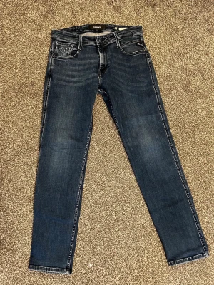 Mörkblå slim fit jeans från Replay - Säljer ett par mörkblå slim fit jeans från Replay med klassisk femficksdesign och snygga slitningar på låren. Jeansen har normal midja och smal passform hela vägen ner. Perfekta för dig som gillar en modern och stilren look. Anbass spegeln var smutsig inte jeansen!!