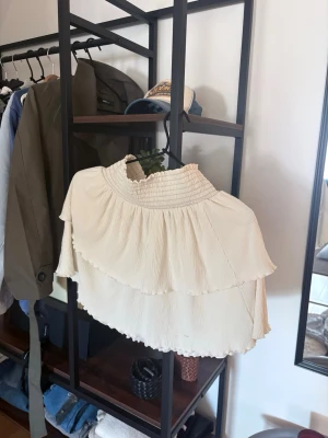 Krämvit volangkjol med resårmidja - Supersöt krämvit kjol med dubbla volanger och bred smockresår i midjan. Kjolen har en luftig och flowy känsla, perfekt för att skapa en romantisk look. Materialet känns lätt och mjukt mot huden.