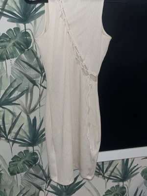 Ribbad vit kortklänning från H&M - Trendig ribbad vit kortklänning från H&M med snörningsdetalj framtill. Klänningen är ärmlös och har en figurnära passform som framhäver siluetten. Perfekt för sommarens alla tillfällen och enkel att styla med accessoarer. Aldrig haft på mig och prislappen sitter kvar.