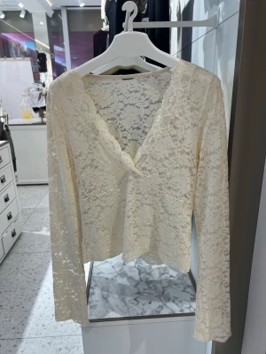 Vit spetsblus med v-ringning - Säljer en superfin vit spetsblus med v-ringning och långa ärmar. Blusen har ett romantiskt spetsmönster över hela plagget och är lätt transparent. Perfekt att styla med jeans eller kjol för en trendig look.
