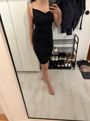Svart klänning SHEIN - Säljer en svart, tight klänning med smala axelband och figurnära passform. Klänningen är kort och har en enkel, stilren design som framhäver siluetten. Perfekt för dig som gillar minimalistisk stil och vill ha en klassisk svart klänning i garderoben.