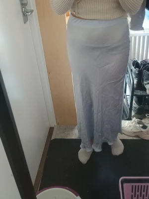 Ljusblå långkjol i satin - Säljer en stilren ljusblå långkjol i satin med mjuk glansig yta. Kjolen har en rak passform och faller snyggt längs benen. Perfekt att matcha med en stickad tröja eller crop top för en trendig look.