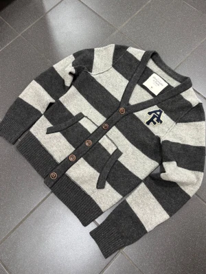 Abercrombie & Fitch kofta - Riktigt schysst Vintage kofta från Abercrombie & Fitch. Snygg logga på bröstet samt ett fint randigt mönster. Bra detalj på de knapparna. Koftan är i ett väldigt bra skick utan några skavanker!😀