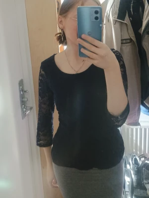Svart spetsblus med trekvartsärm - Säljer en svart blus med eleganta spetsärmar och trekvartsärm. Toppen har en rund halsringning och är figurnära i modellen. Perfekt för dig som gillar stilrena detaljer och vill ha något som sticker ut lite extra.