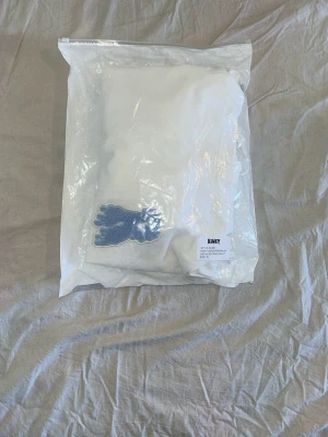 Vit hoodie från Risky med blå patch - Vit hoodie från Risky med stor huva och känguruficka. På bröstet sitter en blå patch i form av ett R med drip-effekt. Tröjan har långa ärmar och snörning vid halsen. Mjuk bomullskänsla och clean look, perfekt för dig som gillar streetwear. ( Helt ny, aldrig använt) väldigt sällsynt tröja 