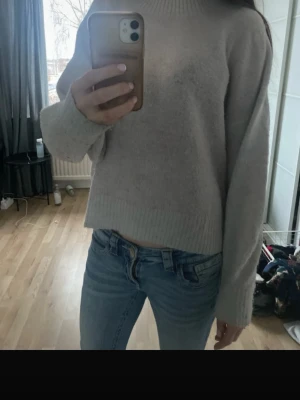 Ljusgrå oversized stickad tröja - Mysig ljusgrå stickad tröja med avslappnad passform och ribbade muddar vid ärmslut och nederkant. Tröjan har en högre rund halsringning och är perfekt för lager på lager. Materialet känns mjukt och skönt mot huden.