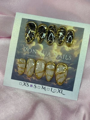 NoirLace (S);Medium Almond - Unika handgjorda press-on naglar. Setet innehåller naglar i svart och vitt med nude bas, dekorerade med lace och abstrakta guldfärgade linjer. Naglarna har en medium lång almondform och en glansig finish som ger en lyxig känsla.S: 15 mm, 11,5 mm, 12 mm, 11 mm, 9 mm 