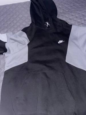 Nike svart och grå hoodie - Snygg hoodie från Nike i svart och grått med klassisk logga på bröstet. Hoodien har huva med dragsko och stor magficka framtill. Perfekt för en avslappnad och sportig stil. Tillverkad i mjukt material för extra komfort. Helt ny oanvänd 