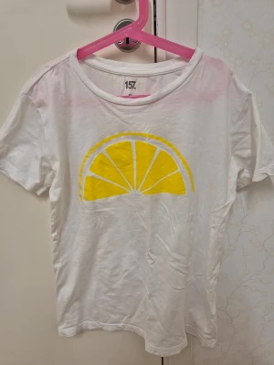 Vit t-shirt med citrontryck från 157 XS - Vit t-shirt från 157 i storlek XS med ett stort gult citrontryck på framsidan. Klassisk rund halsringning och korta ärmar. 