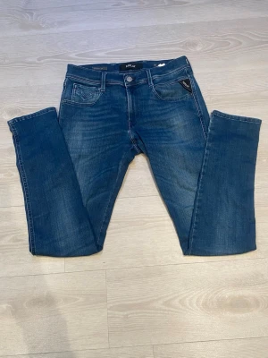 Blå raka jeans från Replay - Mörkblå jeans från Replay med raka ben och klassisk femficksdesign. Jeansen har diskreta slitningar, Replay-logga på bakfickan och en svart läderpatch i midjan. Tillverkade i mjuk denim för en bekväm känsla.