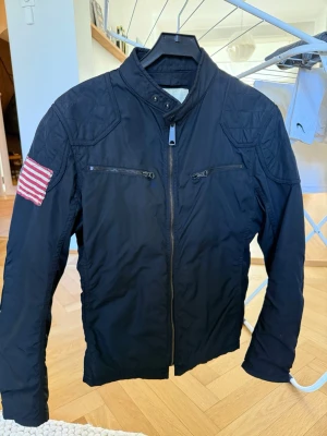 Svart jacka Ralph Lauren - Snygg svart jacka med ståkrage och dragkedja framtill. Två bröstfickor med dragkedja och quiltade axelpartier. Mycket bra skick 