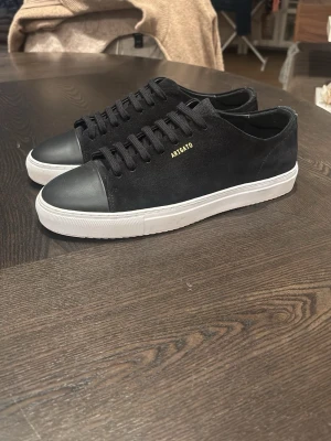 Svarta sneakers från Axel Arigato - Stilrena svarta sneakers från Axel Arigato med ovandel i mocka och tåparti i slätt läder. Skorna har vita, tjocka gummisulor och diskret guldfärgad logga på sidan. Klassisk låg modell med svarta skosnören och minimalistisk design.  Använda typ 1-2 gånger 