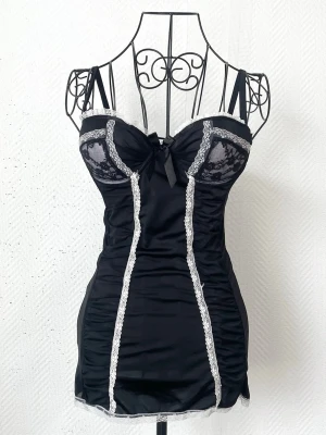 Svart spetsbody med vita detaljer från Rampage Intimates - Snygg svart body med vita spetsdetaljer och dekorativ rosett framtill. Passar storlek XS (32-34), byst under 86cm. Dockans storlek: 34.