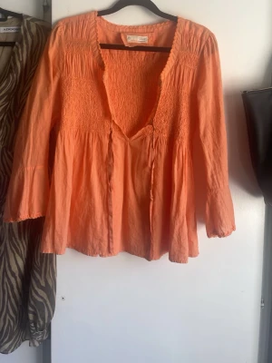 Persikofärgad blus med v-ringning - Säljer en persikofärgad blus från Odd Molly med djup v-ringning och smockdetaljer upptill. Blusen har långa ärmar med lätt utsvängda ärmslut och ett luftigt, flowy material, storleken är one-size men jag skulle säga att detta passar bra för storlek S