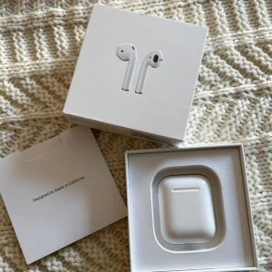 Apple AirPods 2 med laddningsetui - Säljer ett par vita Apple AirPods 2 med trådlöst laddningsetui. Klassisk stilren design i plast, smidiga att ta med överallt. Kommer med originalförpackning och laddkabel. Perfekta för musik, samtal och poddar.