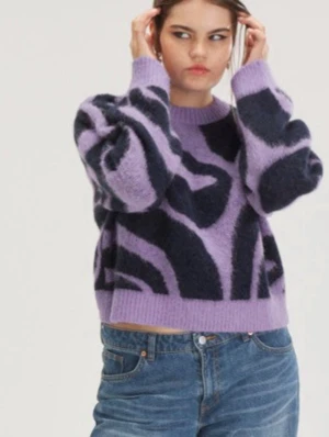 Lila och svart mönstrad stickad tröja från Monki - Säljer en trendig stickad tröja i lila med svart abstrakt mönster från Monki. Tröjan har en boxy passform, rund halsringning och ballongärmar. Materialet ser ut att vara mjukt och fluffigt, perfekt för att hålla värmen. Passar dig som gillar statement-plagg!