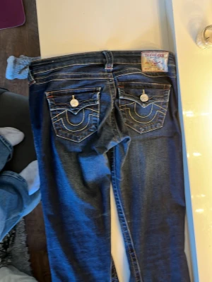 Blå bootcut jeans med broderade fickor - Säljer ett par blå bootcut jeans med snygga broderade detaljer på bakfickorna och kontrastsömmar. Jeansen har klassisk femficksdesign och är tillverkade i slitstark denim. Perfekta för dig som gillar en retroinspirerad look. Ja säljer dom då ja har gått upp i vikt så dom är för små i midjan. Innerbens längden är 75cm