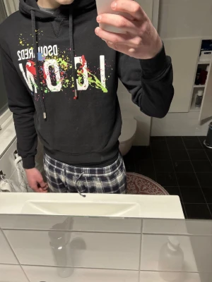 Svart hoodie från Dsquared2 - Snygg svart hoodie från Dsquared2 med färgglada stänk och texten 'ICON' på framsidan. Knappt använd, mycket bra skick! Köpte den i höstas för 4500kr.