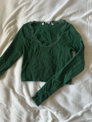 Grön ribbad croppad topp med spets - Snygg grön croppad topp med långa ärmar och ribbad struktur. Urringningen är dekorerad med spetsdetaljer som ger en extra touch