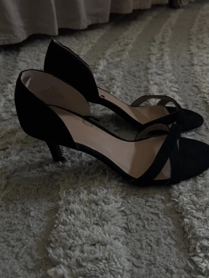 Svarta klackar  - Säljer ett par  svarta klackar från H&M med smala korsade remmar över tårna och öppen häl. Skorna har en låg klack och knappt använda. Sköna och bekväma 