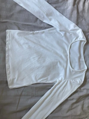 Vit långärmad tröja - En enkel och stilren vit långärmad topp med rundad halsringning. Tillverkad i ett mjukt och stretchigt material som sitter bekvämt på kroppen. Perfekt att matcha med jeans eller kjol för en clean look. Helt oanvänd