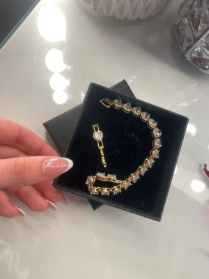 Guldarmband med stora stenar - Snyggt armband i guldton med stora, klara stenar som ger en lyxig känsla. Armbandet har en klassisk design med gnistrande detaljer och matchande hänge. Perfekt för dig som gillar att sticka ut med accessoarer. Vattentät. 