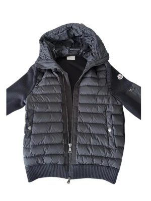 Svart dunväst med huva från Moncler - Snygg svart dunväst från Moncler med stickade ärmar och avtagbar huva. Västen har två fickor med tryckknappar och ribbade muddar. Klassisk Moncler-logga på ärmen och dragkedja framtill. Perfekt tveka inte om du har några frågor och priset kan diskuteras. ✅ alla är originellt bilder det kan se ut lite lilla för solen när jag tog bilden.