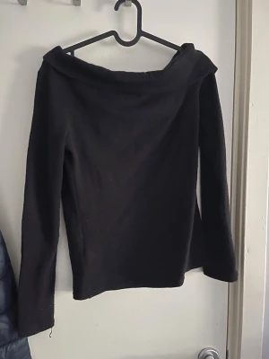 Svart offshoulder topp - Snygg svart offshoulder topp med långa ärmar och bred krage. Perfekt för dig som vill ha en stilren och enkel look. Materialet känns mjukt och stretchigt, vilket gör den bekväm att bära hela dagen.