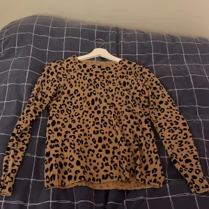 Leopardmönstrad stickad tröja - Snygg stickad tröja med leopardmönster i beige och svart. Tröjan har rund halsringning, långa ärmar och ribbade muddar vid ärmslut och nederkant. Perfekt för dig som vill sticka ut med ett trendigt djurmönster.