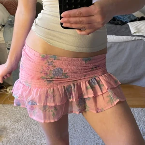 Rosa blommig volangkjol - Supersöt kjol i rosa med blommigt mönster och volangkant. Jag brukar vika ner kjolen utan problem men den kan även användas som en topp. Kjolen har smock i midjan för en bekväm passform och dubbla lager volanger nedtill. Perfekt för dig som vill ha en trendig look.