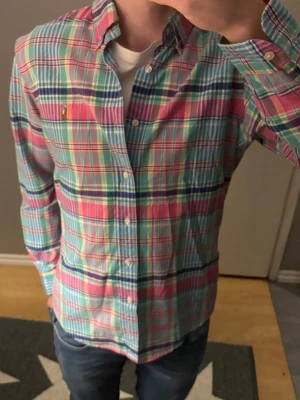 Rutig skjorta från Ralph Lauren M - Säljer min färgglada Ralph lauren skjorta i storlek silmfit M. Passar nog bra på dig om du är runt 180 cm+ och runt 70 kg. Färgen sticker ut bland resterande Ralph lauren skjortor vilket gör att denna skjorta är unik och var därmed dyr för mig när jag köpte den! Priset är ej hugget i sten så hör gärna av dig vid frågor kring priset eller om det är något annat du funderar över kring skjortan🔥