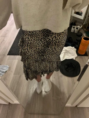 Leopardmönstrad volangkjol - Säljer en snygg leopardmönstrad kjol med volangkant och omlottdetalj. Kjolen har en beige och svart färgskala och är i en längre modell som slutar under knät. Perfekt för dig som vill sticka ut lite extra med ett trendigt mönster. Perfekta till sommaren💝