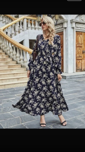 Marinblå Shein klänning - Säljer en superfin marinblå, blommig vardagsklänning från Shein. Klänningen har en markerad midja med knytband och volangdetaljer vid ärmsluten, samt en luftig passform.