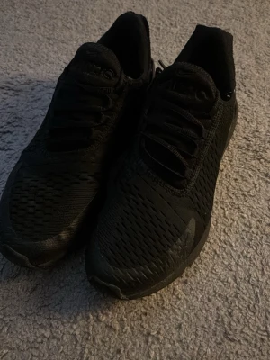 Svarta Nike Air Max sneakers - Säljer ett par helsvarta Nike Air Max sneakers med klassisk luftig mesh och syntetmaterial. Skorna har en chunky sula och diskret Air Max-logga på hälen. Perfekta för dig som gillar sportig och stilren look.