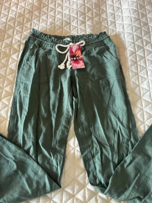 Gröna linnebyxor från Roxy - Snygga gröna linnebyxor från Roxy som sitter väldigt bra på och är lågmidjafe. Säljer då de är lite för långa på mig. Perfekta inför vår och sommar. De är aldrig använda och har därför väldigt bra skick och prislappen kvar. Den här färgen säljs inte längre och de är köpta för 499. Pris går att diskutera☺️💞