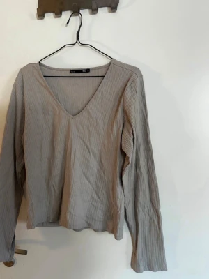 Beige ribbad v-ringad topp lager157 - Säljer en beige ribbad topp från lager157 i storlek XL. Toppen har v-ringning och långa ärmar, perfekt för en chill och enkel look. Materialet är mjukt och stretchigt, vilket gör den skön att bära hela dagen. Rök och djurfritt hem. Pruta gärna!🌸