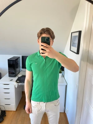 Grön pikétröja från J.Lindeberg - Snygg grön pikétröja från J.Lindeberg med klassisk krage och knappar framtill. Tröjan är tillverkad i 100% bomull, det följer även med en extra knapp. Hör gärna av dig vid frågor!