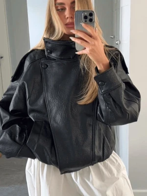 Oversized svart skinnjacka - Säljer en oversized svart skinnjacka med hög krage och asymmetrisk knäppning. Jackan har breda axlar, stora fickor och coola detaljer som knappar vid kragen och axlarna. Perfekt för dig som vill ha en edgy och trendig look.