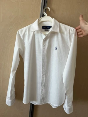 Vit linneskjorta från Ralph Lauren - Klassisk vit linneskjorta från Ralph Lauren med blå broderad logga på bröstet. Toppenskick, inga defekter. Den är storlek M men sitter som S då den krympte när den tvättades. Priset är inte hugget i sten.